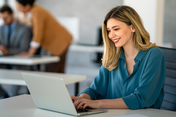 Young happy successful business woman working with laptop in corporate office