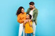 © Prostock-studio - Young parents and daughter posing hugging and smiling to each other standing together on blue background, studio shot