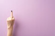 First person top view image of a young woman's hand, adorned with black nail polish, forming an obscene gesture with the middle finger. Captured against a lilac backdrop, leaving room for text or ads