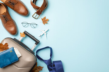 Autumn international business journey theme. Top view of airplane model, belt, fashionable shoes, travel bag, document holder, glasses, maple leaves on soft blue backdrop with space for text or promo