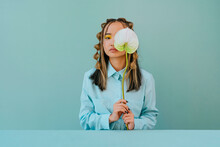 Young Woman Covering Eye With Flower Against Blue Background