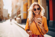 © ty - Beautiful woman wearing yellow sunglasses and bright orange dress walking on the street at sunny day with smartphone