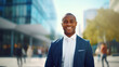 Positive successful African American young businessman in a suit, manager or office worker standing in city center. Male business lifestyle portrait with copy space