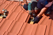 Dachdecker beim Aufbau einer Photovoltaikanlage auf einem neu gedeckten Ziegeldach: Justage und Verschraubung der Halterungen und Klemmen für das Schienensystem an den Dachsparren