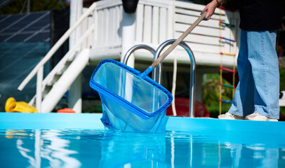 Wall Mural - Young woman cleans swimming pool. Personnel cleaning the pool from leaves in sunny summer day. Hotel staff worker cleaning the pool. Cleaning swimming pool service. Purification with a net. Close up