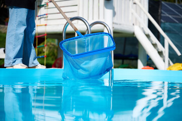 Wall Mural - Young woman cleans swimming pool. Personnel cleaning the pool from leaves in sunny summer day. Hotel staff worker cleaning the pool. Cleaning swimming pool service. Purification with a net. Close up