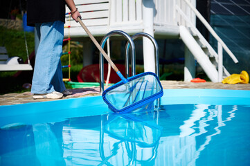 Wall Mural - Young woman cleans swimming pool. Personnel cleaning the pool from leaves in sunny summer day. Hotel staff worker cleaning the pool. Cleaning swimming pool service. Purification with a net. Close up