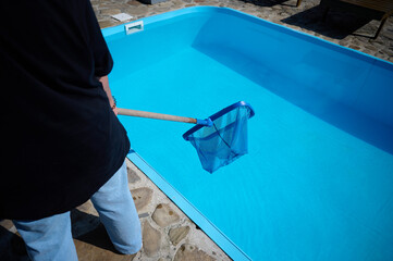 Wall Mural - Young woman cleans swimming pool. Personnel cleaning the pool from leaves in sunny summer day. Hotel staff worker cleaning the pool. Cleaning swimming pool service. Purification with a net. Close up