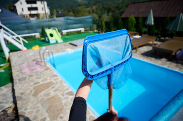 Wall Mural - Young woman cleans swimming pool. Personnel cleaning the pool from leaves in sunny summer day. Hotel staff worker cleaning the pool. Cleaning swimming pool service. Purification with a net. Close up