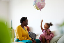 Mother and daughter sitting on sofa, girl playing with balloon