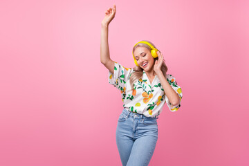 Poster - Portrait of satisfied adorable woman wear stylish print shirt dancing in headphones raising arm up isolated on pink color background