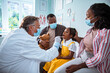 © Marko Geber - Young African American parents supporting their daughter while she is getting tested by a doctor for the coronavirus at the hospital