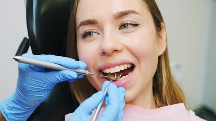 Wall Mural - Woman patient sitting on chair during teeth procedures in dental clinic. Dentist checks front teeth with help of mirror tool and checks strength of teeth