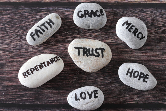 Trust, mercy, faith, grace, love, repentance, and hope handwritten words on stones. Top view. Christian foundation and obedience to God Jesus Christ, biblical concept.