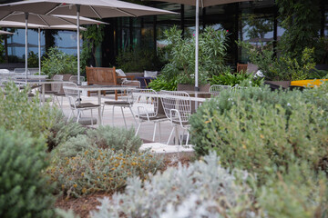 Wall Mural - Modern garden design - Hotel restaurant cafe terrace with a mix of tables and chairs made of different materials as metal, wood, osier, surrounded by pots, green plants and herbs, blurred background