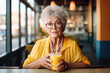 Portrait of serious elderly woman sitting in cafe wearing yellow clothes and drinking juice.
