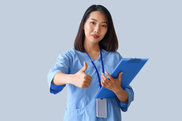 Sticker - Female Asian medical intern with clipboard showing thumb-up on grey background