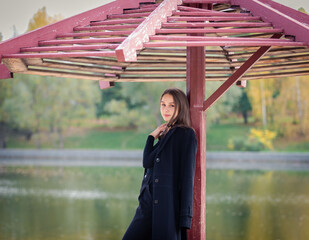 Wall Mural - A beautiful girl poses while standing by a pond under an umbrella in an autumn park.