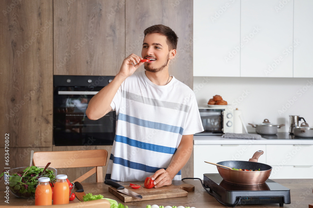 Young man eating cut tomato in kitchen