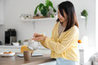 © Pixel-Shot - Beautiful young Asian woman pouring tea from teapot into cup at kitchen
