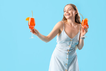 Poster - Beautiful young woman with glasses of tasty aperol spritz cocktail on blue background