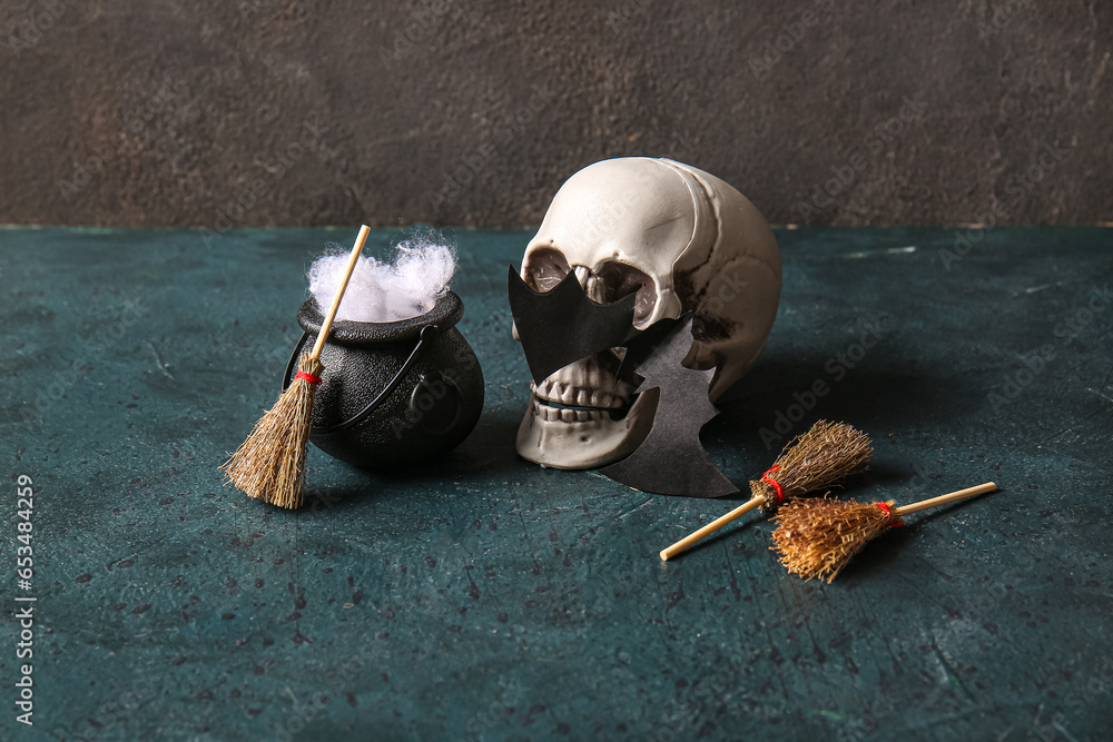 Halloween composition with brooms, skull and cauldron on black grunge background