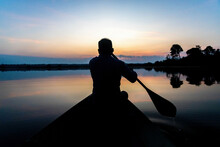 Silhouette Of A Man Paddling Canoe At Dusk Calm Water