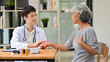 © bongkarn - A professional Asian male doctor is talking with an old lady patient in an examination room.