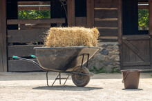 A Wheelbarrow Loaded With Hay In Front Of A Barn