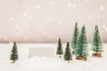 White pedestal for cosmetics and care products on artificial snow, artificial Christmas trees against a background of blurry lights. Cosmetics Christmas gifts concept. Selective focus.