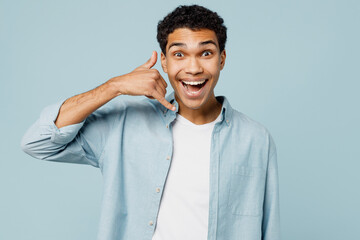 Wall Mural - Young surprised man of African American ethnicity wear shirt white t-shirt casual clothes do phone gesture like says call me back isolated on plain pastel light blue cyan background studio portrait