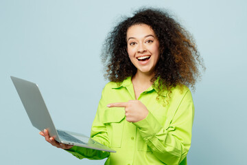 Cheerful smiling young IT latin woman wear green shirt casual clothes hold use work point on laptop pc computer isolated on plain pastel light blue cyan background studio portrait. Lifestyle concept.