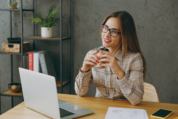 Wall Mural - Young minded employee business woman wear shirt casual clothes glasses sit work at office desk with pc laptop hold takeaway delivery craft paper brown cup coffee to go. Achievement career job concept.