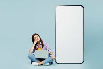 Wall Mural - Full body young fun woman wears purple shirt yellow t-shirt casual clothes big huge blank screen mobile cell phone smartphone with area use laptop pc computer isolated on plain light blue background.