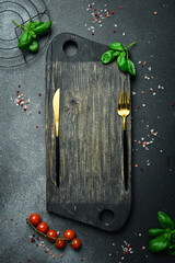 Wall Mural - Creative kitchen banner. Cutting board, cutlery, spices and kitchen utensils on black stone background. Free space for text.