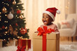 © Jim1786 - Excited, surprised, shocked, wondered Christmas Child opening present, portrait Happy African American baby Boy smiling in Santa Claus hat with giftbox at home.