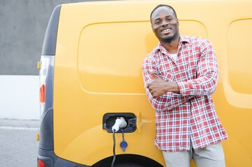 Wall Mural - A african american man stands next to yellow electric delivery van at electric vehicle charging stations