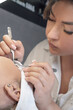 © Евгения Рубцова - Lashmaker performing procedure of eyelash extension, carefully sticking fake lashes using tweezers sitting over client.