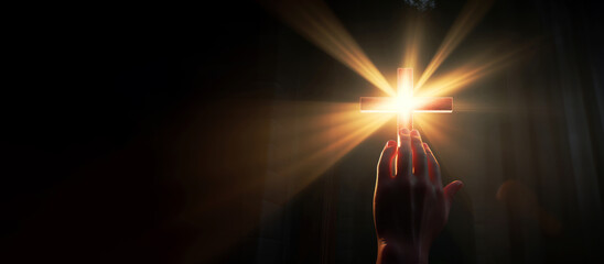 Canvas Print - Hand reaching for the cross with light rays on a dark background. Copy space