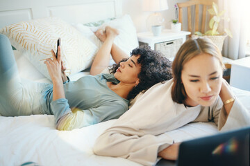 Poster - Lesbian, couple and bed with laptop and phone for streaming movie or internet for relax, connection or online. Lgbt woman, reading and lens flare home for social media or subscription in bedroom