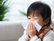 Sick asian boy blowing her nose with flu symptoms coughing on sofa at home