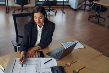 Wall Mural - Smiling female architect engineer working with documents project sitting desk in office