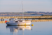 A Fishing Trawler Sitting In A Calm Marina In Front Of A Road Bridge