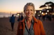 Portrait of happy senior woman looking at camera and smiling while standing against a sunset in a paradise beach. Freedom, peace, relax, holiday concept