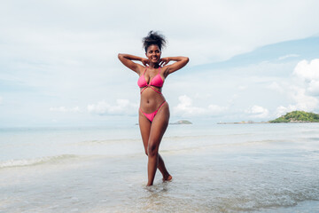 Sticker - Beautiful African american woman in pink bikini on tropical beach. Portrait of dark skinned woman smiling at sea. Brunette tanned girl in swimwear enjoying and walking on beach.