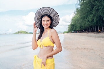 Wall Mural - Beautiful woman in yellow bikini on tropical beach. Portrait of happy young woman smiling at sea. Brunette tanned girl in swimwear enjoying and walking on beach.