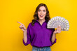 Photo of impressed excited woman with curly hairdo dressed purple shirt hold dollars indicating empty space isolated on yellow background