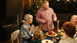 © TrueFrame Collective - High angle of mature Caucasian man bringing roasted turkey to festive table for Christmas dinner and starting to cut it
