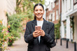 Sunny portrait of a newly entrepreneur young woman in her 25s, black suit, holding a phone smiling, looking in camera