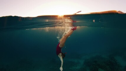 Wall Mural - Woman freediver dives underwater to explore the underwater world of the Komodo National Park in Indonesia at sunset